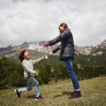 Woman and Child Playing on Green Grass Field Near Mountain